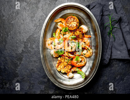 Grilled fried Shrimps Prawns on oval metal plate. Dark background. Top view Stock Photo