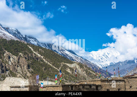 Multi-colored flags above the roofs of houses and against the snowy mountains in the Himalayas, Nepal. Stock Photo