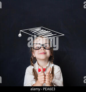 Little genius kid in  graduation hat with thumb up on chalkboard Stock Photo