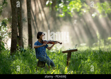 The girl is enjoying playing the violin or playing his music in the wild. Stock Photo