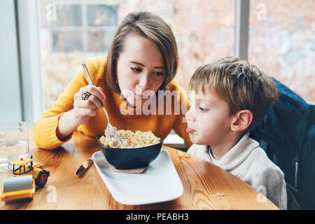 Portrait of white Caucasian happy family, mother and son, sitting in restaurant cafe at table, feeding eating pasta spaghetti, authentic lifestyle Stock Photo