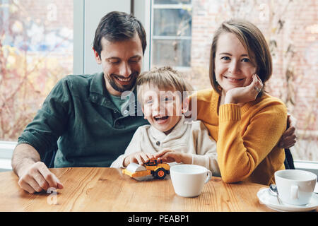 Portrait of white Caucasian happy family of three mother, father and son, sitting in restaurant cafe at table, smiling playing, authentic lifestyle Stock Photo