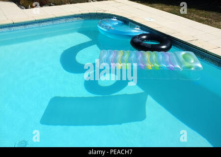 Swimming pool inflatables throwing shadows on the blue pool water in France. 2018. Stock Photo