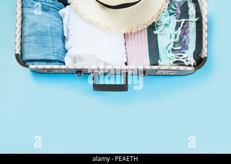 Open suitcase with female clothes for trip on pastel blue. Top view with copy space. Summer concept travel. Stock Photo