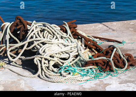 Rope and anchor chain on the edge of the mooring. A concrete edge, behind her bright blue sea water Stock Photo