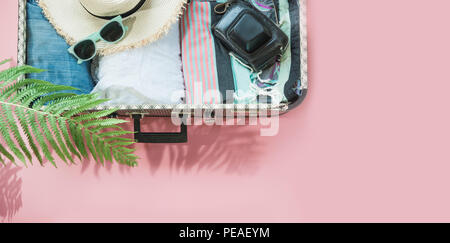 Open suitcase with female clothes for trip on pastel pink. Top view with copy space. Summer concept travel. Stock Photo