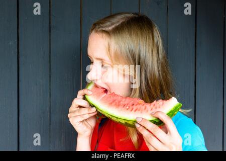A beautiful and young girl bites open her mouth fresh, delicious and juicy watermelon. She is very hungry and wants to eat it. Stock Photo