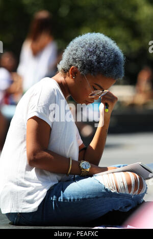 NEW YORK, NY - SEPTEMBER 02: Young black woman studying a book while sitting in Washington Square Park, Manhattan on September 2, 2016 in New York, US Stock Photo