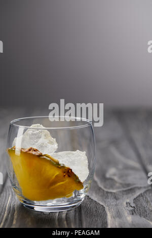glass with ice cubes and piece of pineapple on grey wooden table Stock Photo