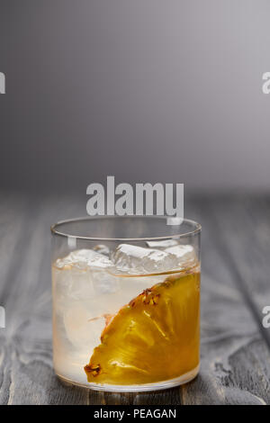 glass of lemonade with pineapple piece and ice cubes on grey wooden table Stock Photo