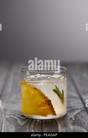 glass of lemonade with rosemary, ice cubes and pineapple on grey wooden table Stock Photo