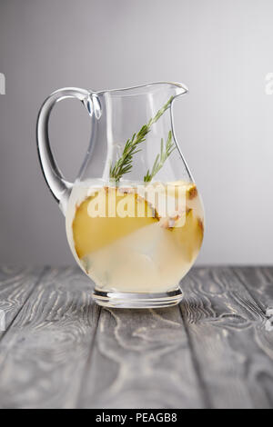 jug of lemonade with rosemary and pineapple pieces on grey wooden tabletop Stock Photo