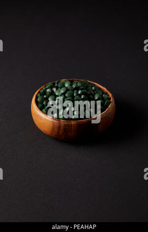 wooden bowl with pile of spirulina pills on grey table Stock Photo