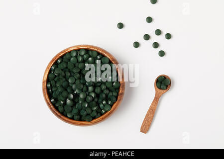 elevated view of wooden spoon and bowl with pile of spirulina pills on grey table Stock Photo