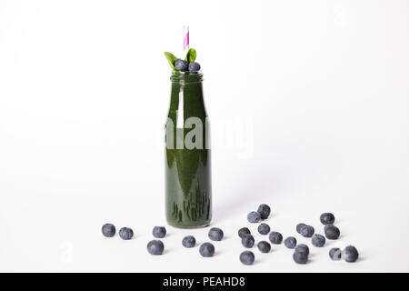 bottle of spirulina smoothie with leaves and drinking straw surrounded by blueberries on white background Stock Photo