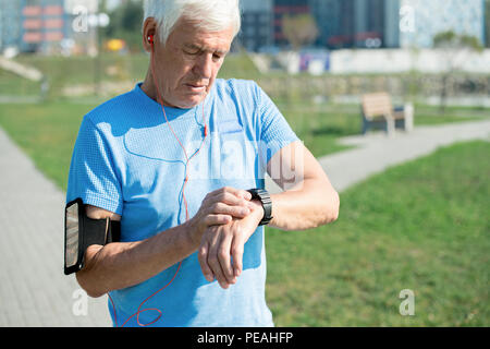 Waist up portrait of modern senior man setting up smart watch and listening to music while doing morning run in park, copy space Stock Photo