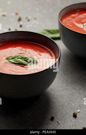 two plates with tasty tomato soup and basil on grey table Stock Photo