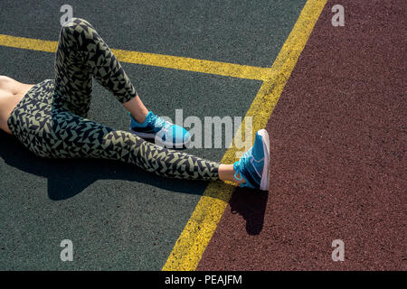 High angle portrait of unrecognizable  young woman resting lying on ground in outdoor basketball court in sunlight, copy space Stock Photo