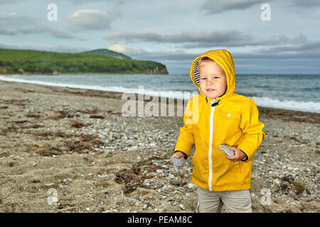 Cute boy in yellow jacket with hood on the pebble beach