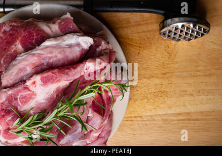 Pieces of raw pork steak with rosemary and butcher hummer, on dark wooden background in rustic style Stock Photo