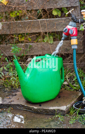Water being taken from a tap with a hose pipe and watering can. Stock Photo