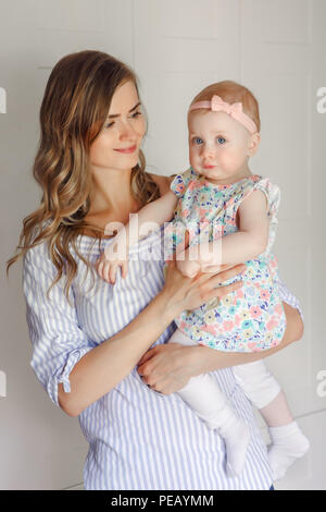 Closeup portrait of beautiful white Caucasian woman mother holding cute adorable blonde baby girl daughter with large blue eyes,  family lifestyle, mo Stock Photo