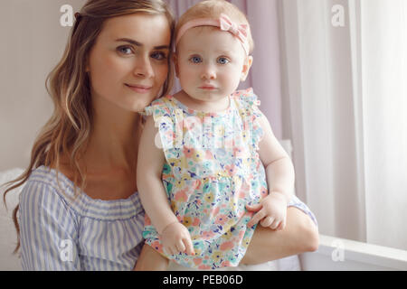 Closeup portrait of beautiful white Caucasian woman mother holding cute adorable blonde baby girl daughter with large blue eyes looking in camera,  fa Stock Photo