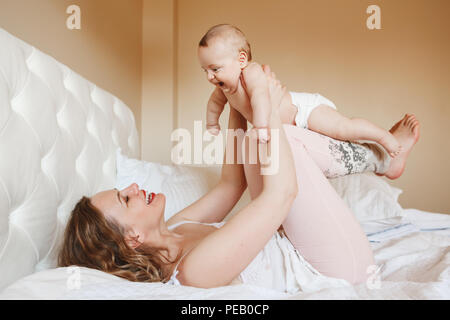 Group portrait of beautiful middle age white Caucasian mother and baby together on bed in bedroom doing physical fitness exercises yoga together, earl Stock Photo