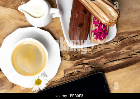 wooden plate with Coffe eclairs with cup of fresh black coffee, pitcher of cream, and coffee beans on Top view. Stock Photo