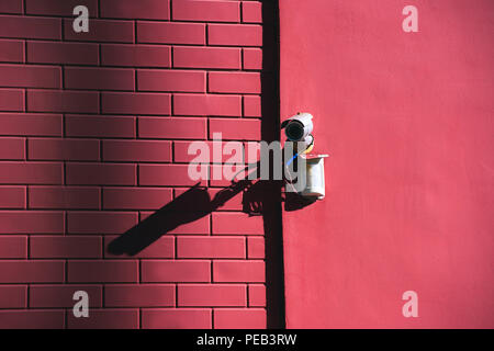 close up view of security camera on pink building facade in sunlight Stock Photo