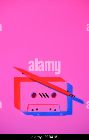 toned pink picture of retro audio cassette and pencil on tabletop Stock Photo