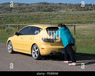 Hispanic woman pushing a compact yellow car after it has broken down in a rural area. Stock Photo