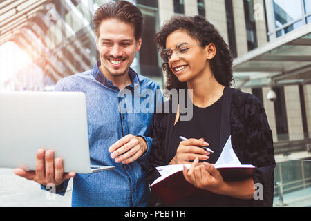 Two smiling colleagues are chatting in the street during lunch break near the building in the background. Stock Photo