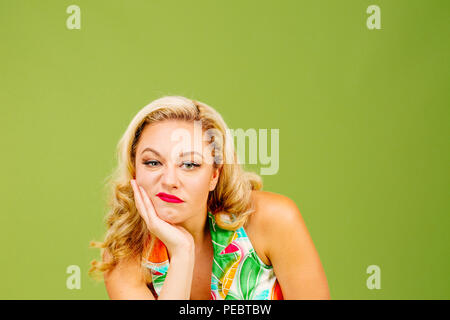 Portrait of a bored and unhappy blonde woman, isolated on green studio background Stock Photo