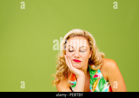 Portrait of a grumpy blonde woman looking down, isolated on green studio background Stock Photo