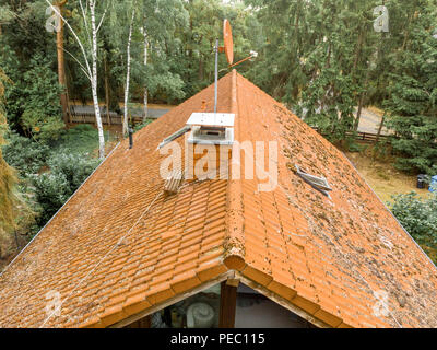 Inspection of the red tiled roof of a detached house, with a covered chimney and a satellite antenna Stock Photo