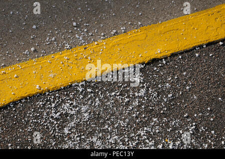 Road salt grit / rock salt / sodium chloride scattered around a painted yellow line Stock Photo