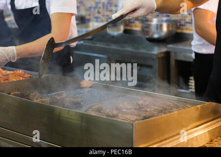 Man fries meat and burger cutlets on a steaming grill Stock Photo