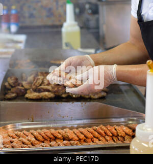 Man fries meat and burger cutlets on a steaming grill Stock Photo