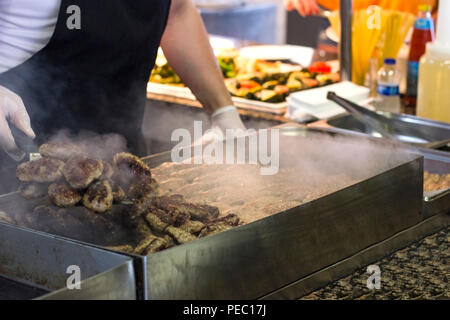 Man fries meat and burger cutlets on a steaming grill Stock Photo