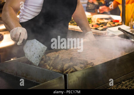 Man fries meat and burger cutlets on a steaming grill Stock Photo