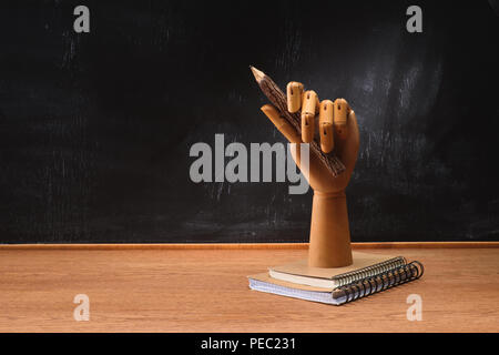 close up view of textbooks under wooden hand holding pencil on desk in front of chalkboard in school Stock Photo
