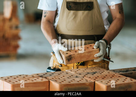 cropped image of construction worker in protective gloves holding brick at construction site Stock Photo