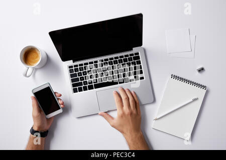cropped shot of man working with laptop and holding smartphone in hand on white surface for mockup Stock Photo