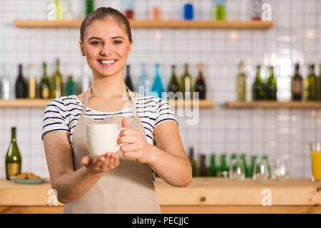 Coffee bar. Nice positive young woman smiling and holding a cup filled with delicious coffee while working in the coffee bar Stock Photo