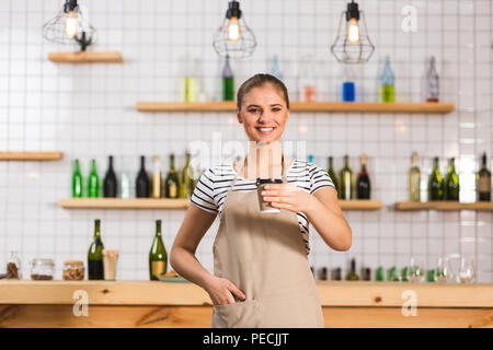 Takeaway coffee. Positive cheerful female barista standing in the cafe and smiling while holding a plastic cup with coffee Stock Photo