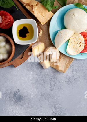 Italian cheeses. Mozzarella Buffalo, crottin, balls, Stracciatella, basil leaves, tomatoes, olive oil with vinegar on gray background. Top view, copy space. Stock Photo