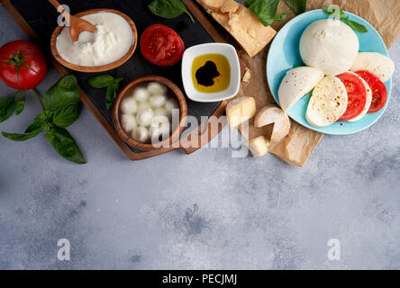 Italian cheeses. Mozzarella Buffalo, crottin, balls, Stracciatella, basil leaves, tomatoes, olive oil with vinegar on gray background. Top view, copy space. Stock Photo