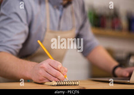 Small notes. Selective focus of a pencil being used by a pleasant nice man for taking notes while working in the cafeteria Stock Photo