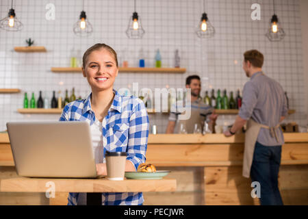 At lunch. Joyful nice beautiful woman sitting at the laptop and having lunch while visiting a cafe Stock Photo